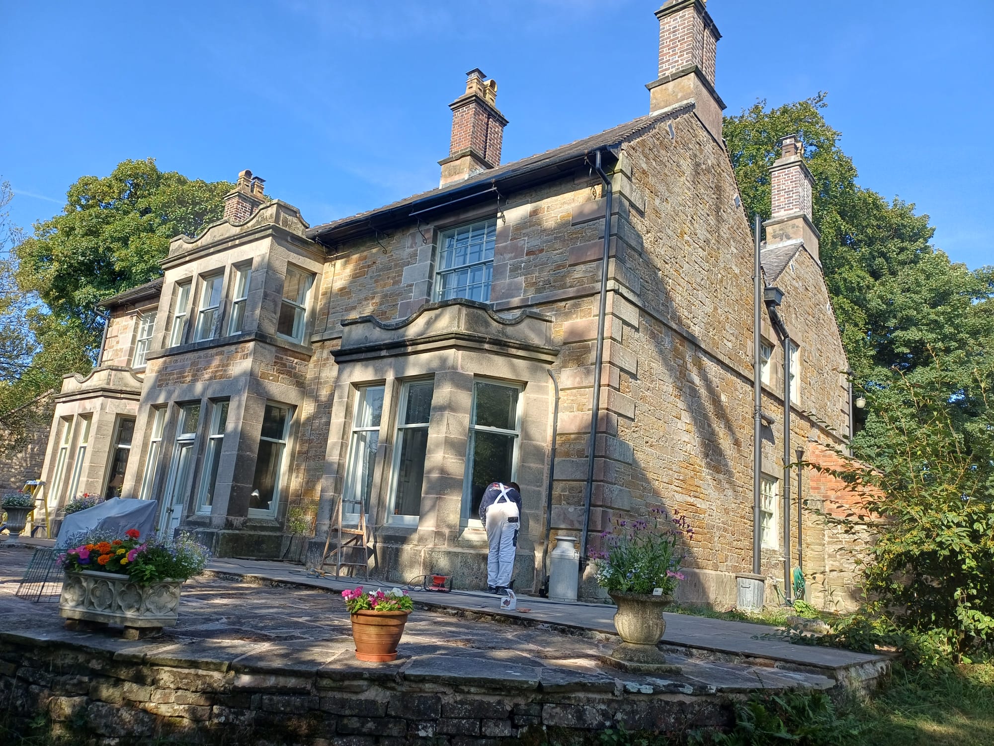 Decorator in white overalls painting the windows of a large stone house