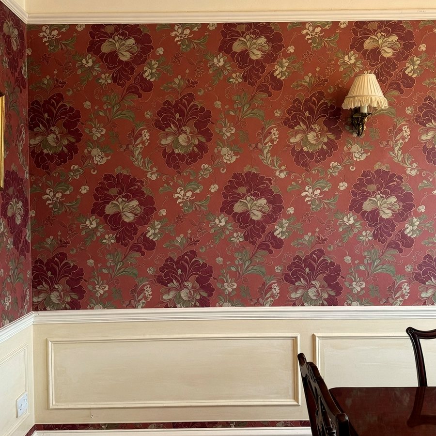 Dining room wall finished in large floral wallpaper above painted panelling